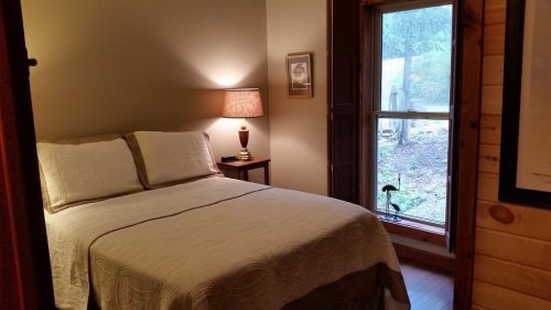 Cozy bedroom with a double bed, bedside lamp, and a window overlooking a garden. Warm, inviting atmosphere.