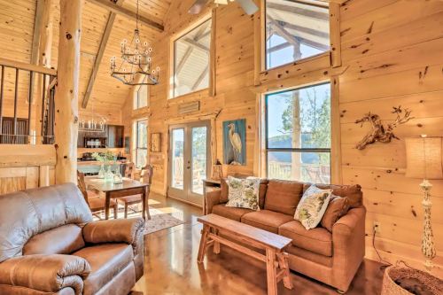 Cozy wooden living room with large windows, a sofa, and a dining area, featuring rustic decor and scenic views.