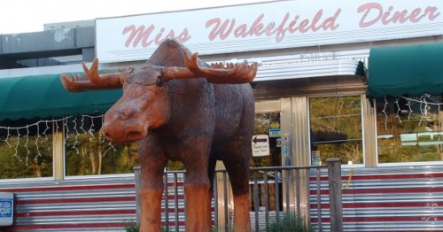 A large wooden moose statue stands in front of the Miss Wakefield Diner, featuring a retro-style exterior.