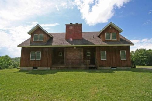 A rustic wooden house with a chimney, set against a blue sky and green lawn.