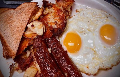 A plate of breakfast featuring two fried eggs, sausage links, crispy potatoes, and toasted bread.