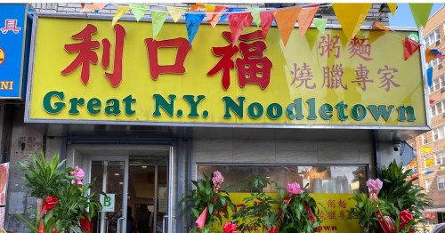 A colorful restaurant sign reads "Great N.Y. Noodletown" with decorative flags and plants in front.
