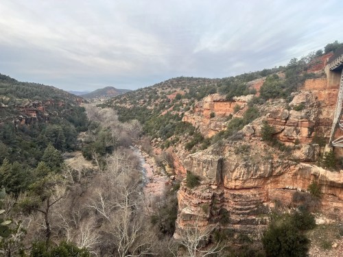 A scenic view of a canyon with rocky cliffs, a winding river, and trees under a cloudy sky.