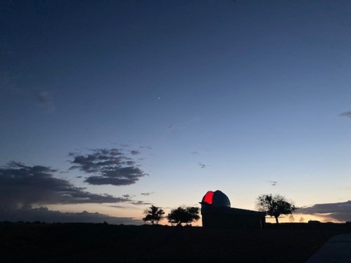 Silhouette of an observatory against a twilight sky, with trees and clouds in the background.