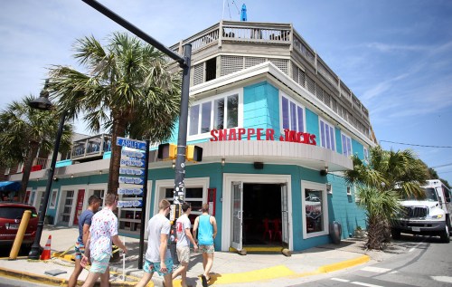 A colorful beachside restaurant named Snapper Jacks, with palm trees and people walking by on a sunny day.