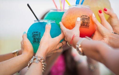 A group of hands holding colorful cocktails in large glasses, celebrating together.