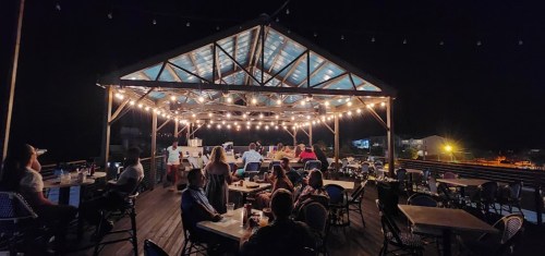 A lively rooftop restaurant at night, with string lights and patrons enjoying food and drinks at tables.
