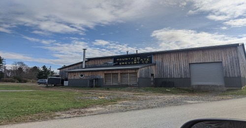 A rustic brewery building with a wooden exterior and a sign reading "Mountain State Brewing Co." under a cloudy sky.
