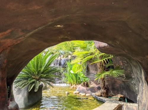 A serene view through a stone archway, showcasing lush greenery and a small waterfall in a tranquil setting.