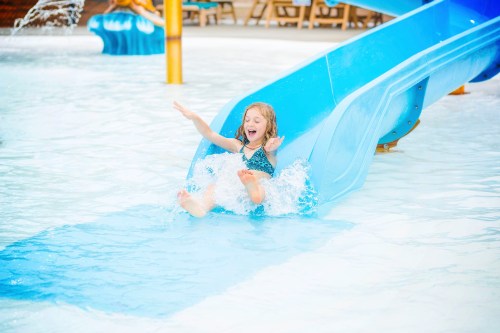 A joyful child slides down a blue water slide, splashing into a pool at a water park.