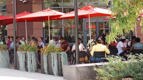 A bustling outdoor dining area with red umbrellas, filled with people enjoying their meals at tables.