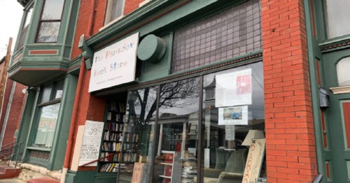 Exterior of a red brick building featuring a bookstore with large windows and a sign that reads "The Paradox Book Store."