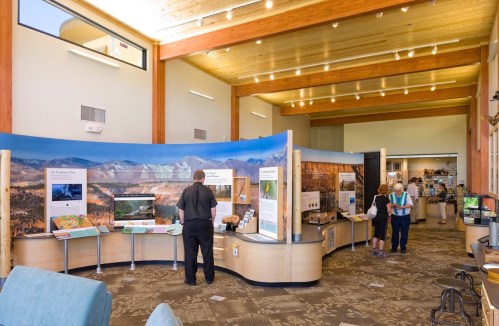 Interior of a visitor center with informational displays about nature, people exploring exhibits, and a bright, open space.