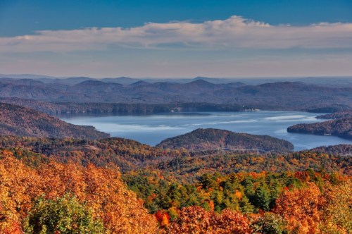 A scenic view of a lake surrounded by mountains, showcasing vibrant autumn foliage under a clear blue sky.