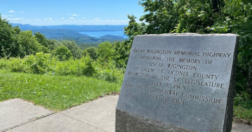 A stone monument honoring Oscar Wigington, with a scenic view of mountains and a lake in the background.