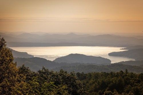 A serene landscape featuring a lake surrounded by mountains, illuminated by a warm, golden sunset.