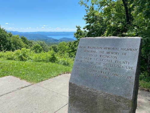 A stone monument honoring Oscar Wigington, with a scenic view of mountains and a lake in the background.