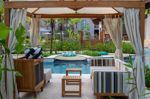 A cozy outdoor seating area with a view of a pool, surrounded by greenery and modern architecture.