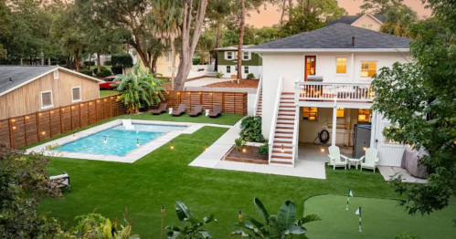 Aerial view of a backyard with a pool, green lawn, and a two-story house surrounded by trees and outdoor seating.