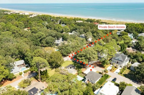 Aerial view of a coastal neighborhood with a marked path leading to private beach access. Lush greenery surrounds the homes.