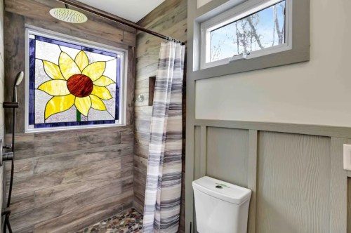 Bright bathroom featuring a stained glass sunflower window, wooden walls, a shower, and a modern toilet.