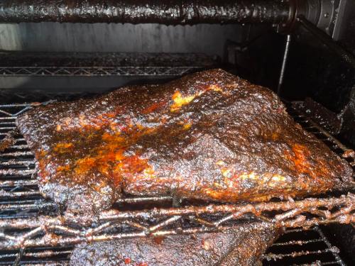 A close-up of a smoked brisket on a grill, showcasing a dark, caramelized crust and juicy texture.