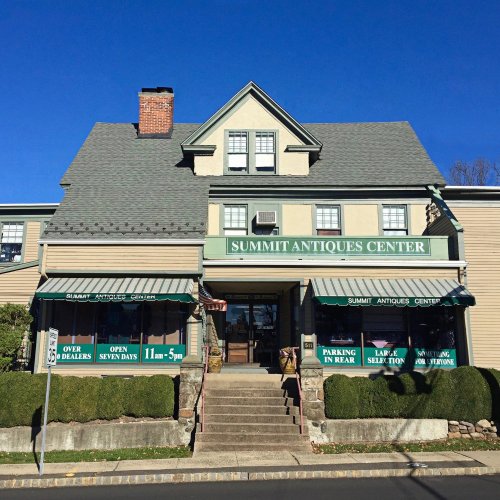 A large, two-story building with a green awning reading "Summit Antiques Center," surrounded by neatly trimmed hedges.