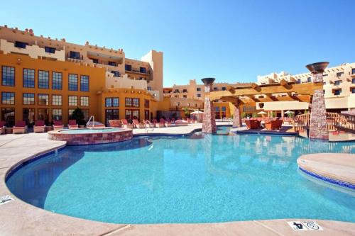 A sunny pool area with lounge chairs, surrounded by a colorful building and clear blue sky.