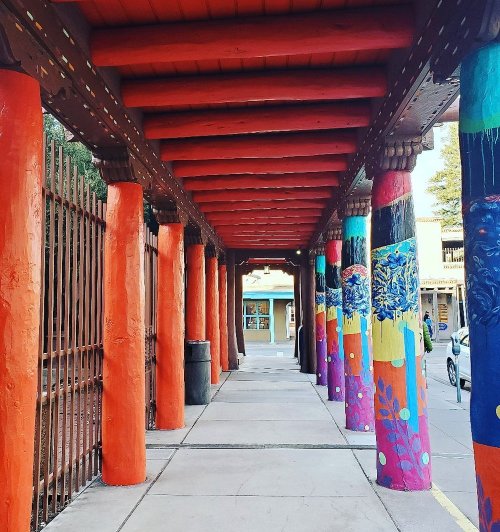Colorful columns with murals line a walkway, leading to a building in a vibrant, artistic setting.