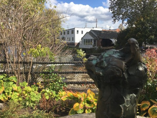 A bronze sculpture in the foreground with a view of a river and buildings in the background under a partly cloudy sky.