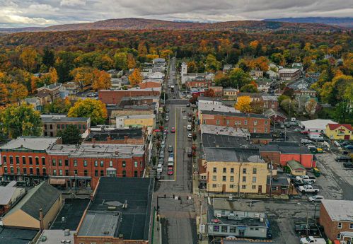 Aerial view of a small town with colorful autumn trees, featuring streets lined with buildings and parked cars.