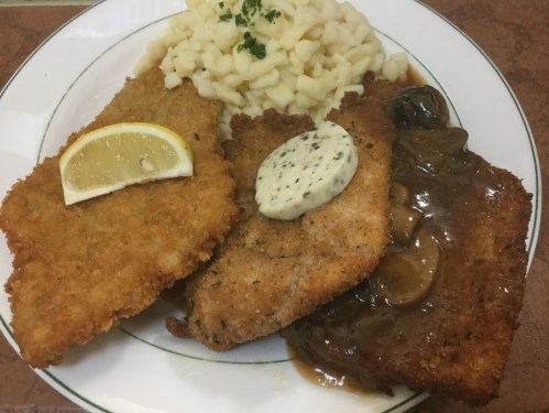 A plate featuring three breaded meat cutlets, one with lemon, one with sauce, and a side of mashed potatoes.