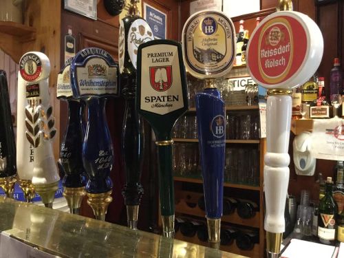 A row of beer taps featuring various brands, including Spaten and Reissdorf Kölsch, in a bar setting.