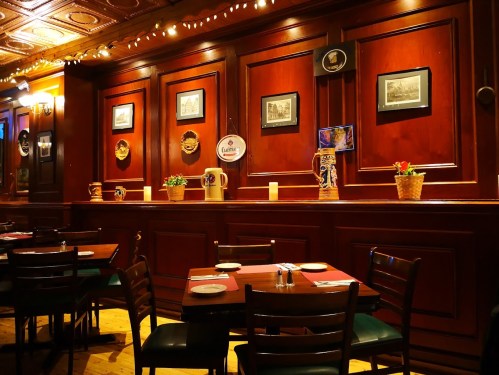 Cozy restaurant interior with wooden walls, framed pictures, and tables set for dining under warm lighting.