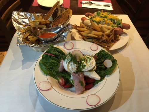 A table setting with a salad topped with ham and herbs, a plate of fries, and a side of dipping sauce.