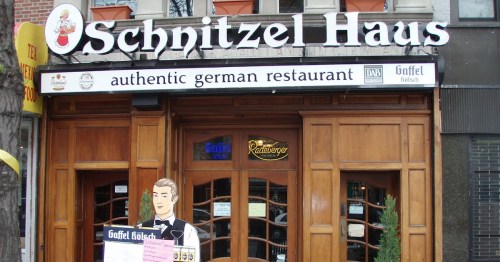 Exterior of Schnitzel Haus, an authentic German restaurant, featuring wooden doors and a sign above.