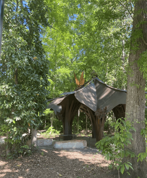 A unique, artistic pavilion surrounded by lush green trees in a serene outdoor setting.