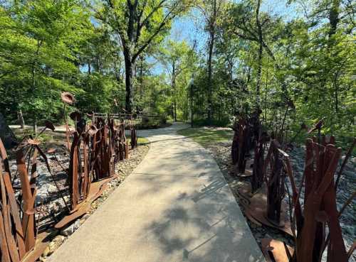 A winding path through a lush green forest, flanked by artistic metal sculptures.