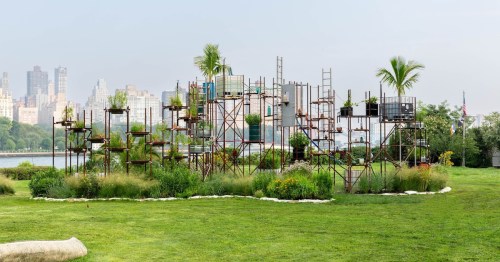 A modern garden structure with plants, set against a city skyline and green grass.