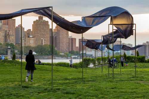 A park scene with flowing fabric structures, city skyline in the background, and people enjoying the outdoors.