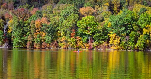 Fishing boat on calm water at Clendening Lake in Ohio, surrounded by vibrant autumn foliage, reflecting on the water.