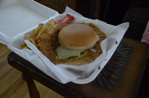 A takeout container with a fried chicken sandwich, lettuce, and fries on a wooden table.