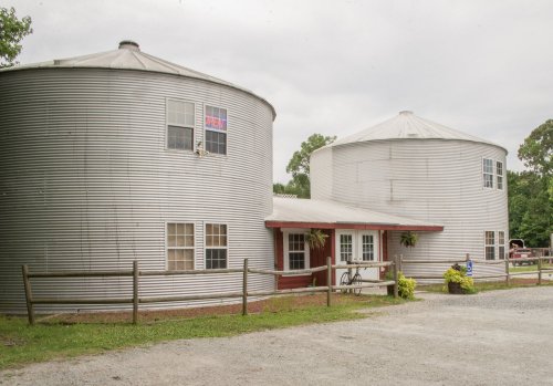 Two large silos converted into a house, with a red door and greenery, set against a cloudy sky.