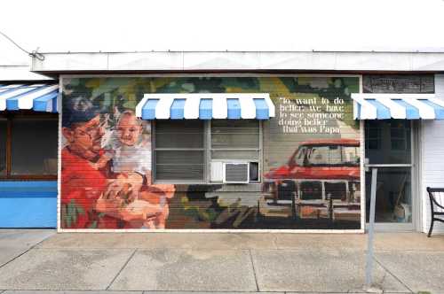 A colorful mural on a brick wall depicts a man with a baby, alongside a vintage car and a heartfelt message.