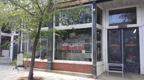 Exterior of a vintage shop with large windows displaying "American Pickers" sign, surrounded by trees and brick facade.