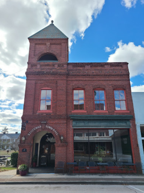 Historic red brick building with a tower, featuring large windows and a welcoming entrance, under a blue sky with clouds.