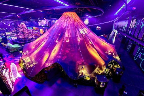 A vibrant, illuminated tent resembling a volcano, surrounded by colorful lights and decorations in a large indoor space.