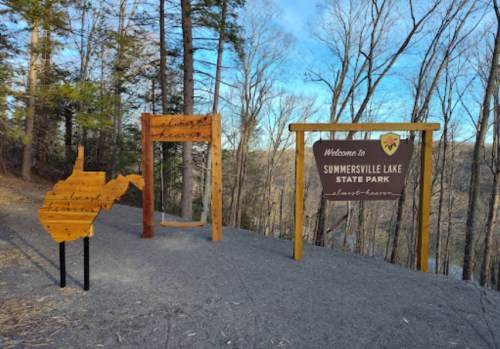 Welcome sign for Summersville Lake State Park, featuring wooden structures and a map outline of West Virginia.