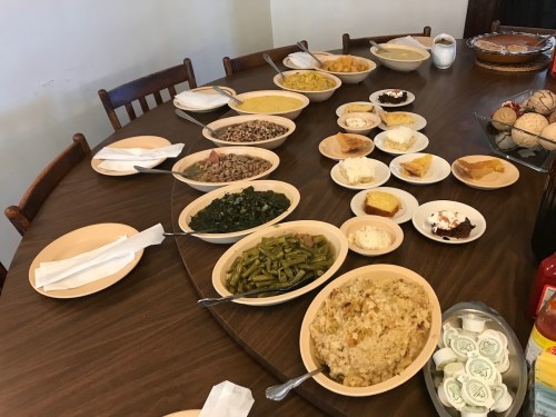 A table set with various dishes, including rice, beans, greens, desserts, and condiments, ready for a meal.