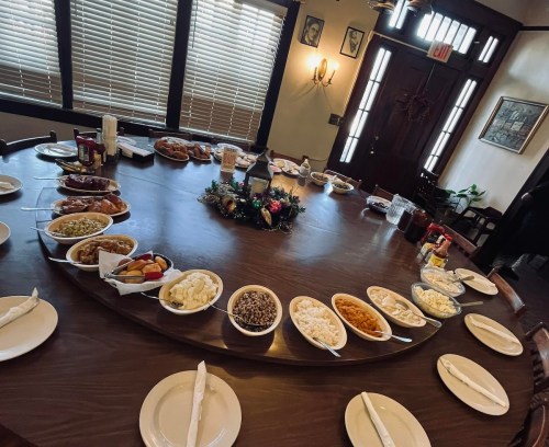 A round table set with various dishes, including sides and desserts, ready for a meal in a cozy dining room.